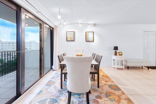 dining room with track lighting, a textured ceiling, crown molding, light tile patterned floors, and baseboards