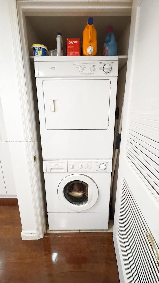 clothes washing area with stacked washer / drying machine, wood finished floors, and laundry area