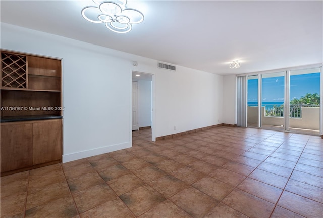 empty room with baseboards, visible vents, a wall of windows, and tile patterned floors