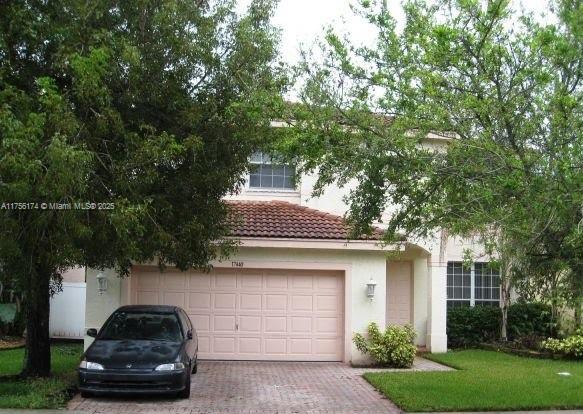 view of front of house featuring a garage, a tiled roof, decorative driveway, stucco siding, and a front lawn