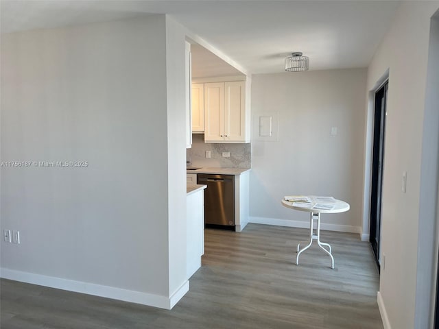 kitchen featuring tasteful backsplash, light countertops, white cabinets, dishwasher, and baseboards