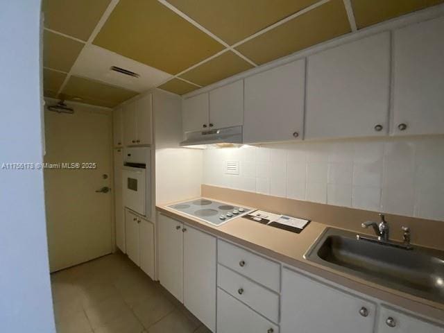 kitchen featuring tasteful backsplash, white cabinets, a sink, oven, and under cabinet range hood