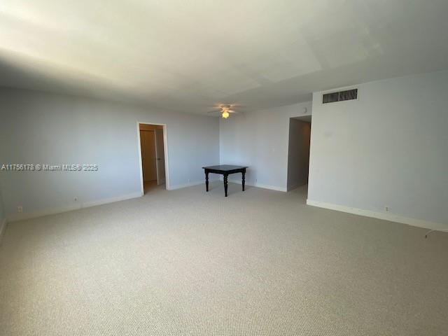 empty room featuring light carpet, ceiling fan, visible vents, and baseboards