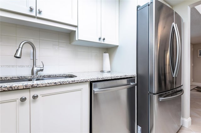 kitchen with backsplash, appliances with stainless steel finishes, white cabinetry, a sink, and light stone countertops