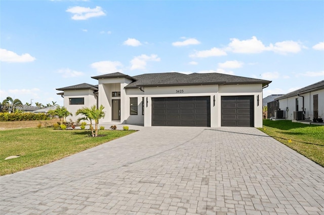 prairie-style home featuring a front lawn, cooling unit, decorative driveway, and an attached garage