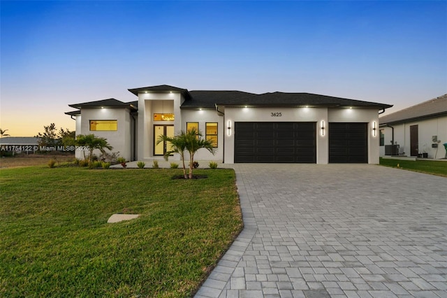 prairie-style house with an attached garage, stucco siding, decorative driveway, and a front yard