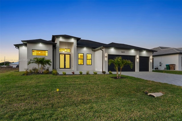 prairie-style home with a garage, a front lawn, decorative driveway, and stucco siding