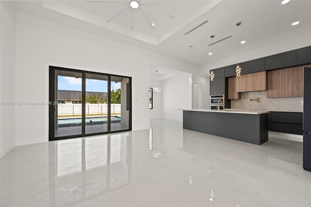 kitchen featuring a tray ceiling, light countertops, a center island with sink, and modern cabinets