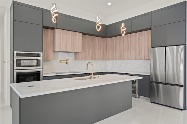 kitchen featuring stainless steel appliances, tasteful backsplash, a sink, an island with sink, and modern cabinets