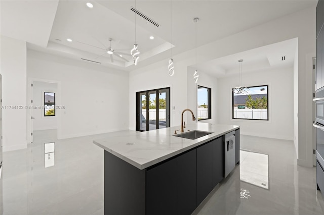 kitchen featuring a center island with sink, a raised ceiling, open floor plan, a sink, and dark cabinetry