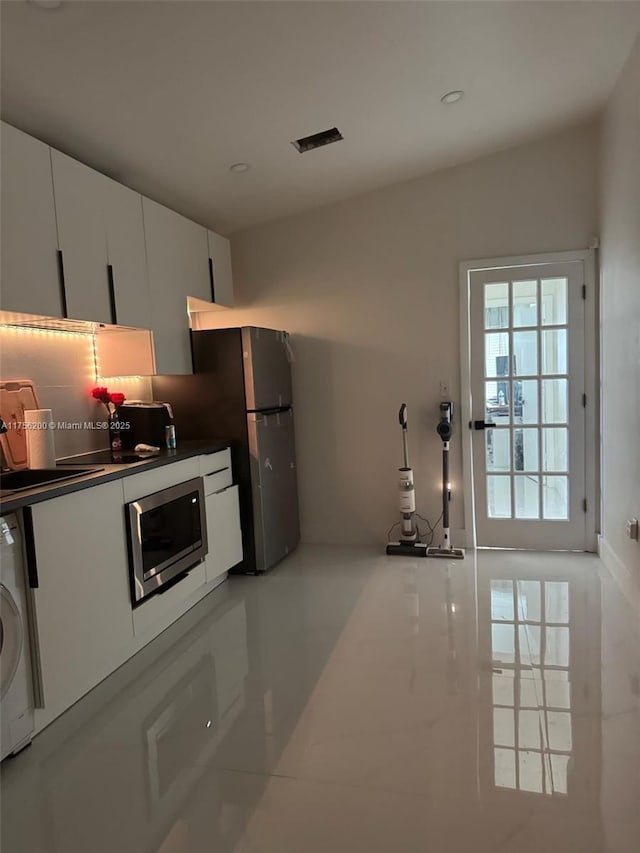 kitchen featuring tasteful backsplash, dark countertops, washer / clothes dryer, stainless steel appliances, and white cabinetry