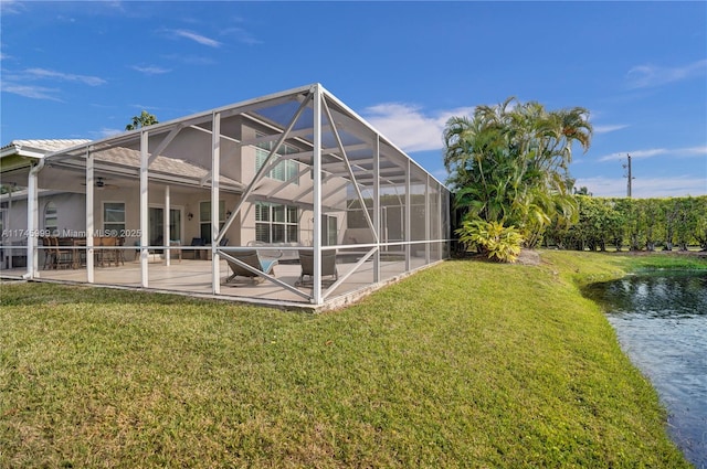 rear view of property with a yard, a patio, a water view, a ceiling fan, and glass enclosure