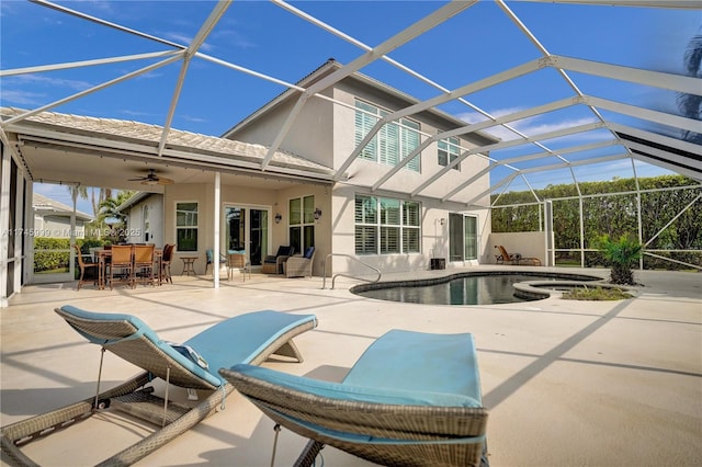 exterior space with stucco siding, glass enclosure, a patio area, ceiling fan, and an in ground hot tub