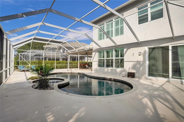view of pool featuring glass enclosure, a pool with connected hot tub, ceiling fan, and a patio