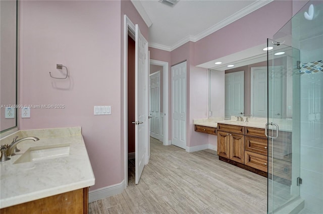 bathroom with wood finished floors, two vanities, a sink, ornamental molding, and a shower stall