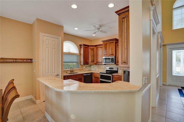 kitchen with appliances with stainless steel finishes, brown cabinets, a sink, and light tile patterned flooring