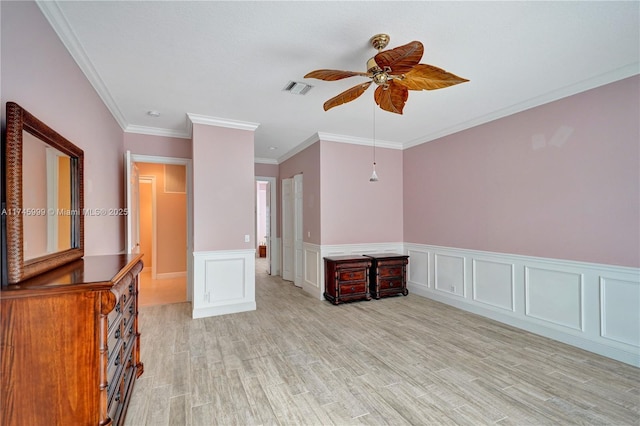 spare room featuring ceiling fan, ornamental molding, visible vents, and light wood-style floors