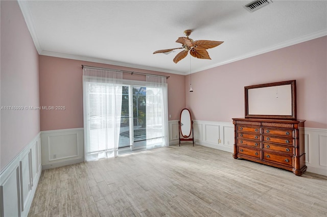 unfurnished room with ceiling fan, a decorative wall, wood finished floors, visible vents, and crown molding
