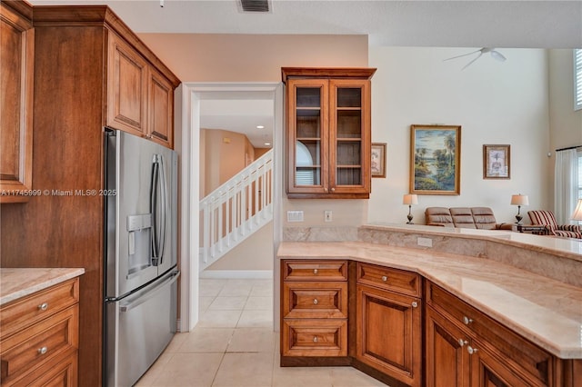 kitchen with light tile patterned floors, visible vents, brown cabinetry, stainless steel fridge, and glass insert cabinets