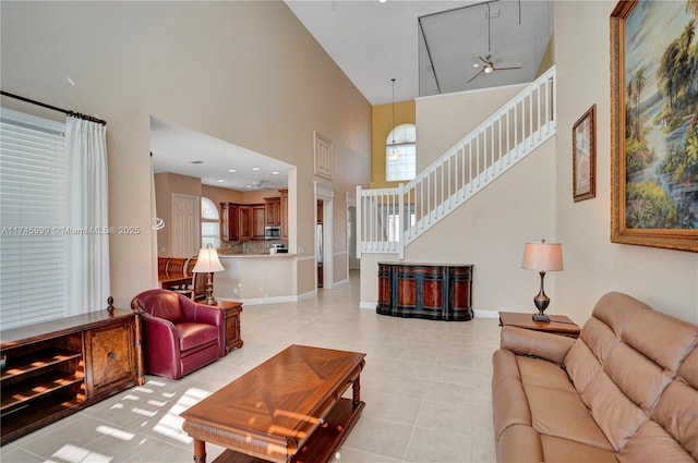 living area featuring light tile patterned floors, baseboards, a ceiling fan, a towering ceiling, and stairs