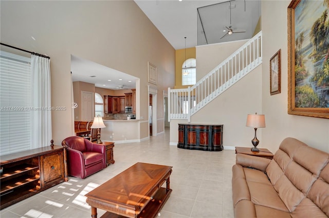 living area featuring light tile patterned floors, stairway, a towering ceiling, ceiling fan, and baseboards