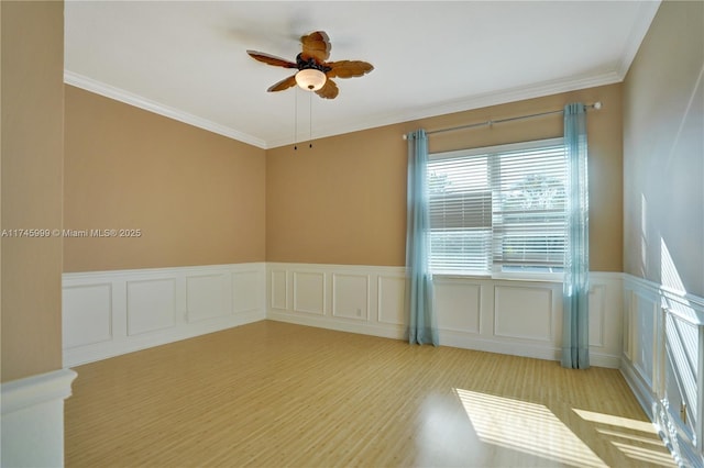 empty room featuring a wainscoted wall, ceiling fan, crown molding, and wood finished floors