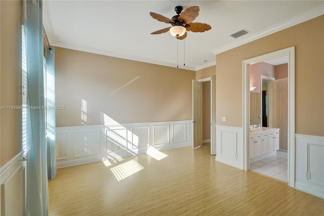 spare room featuring crown molding, visible vents, a decorative wall, a sink, and light wood-type flooring