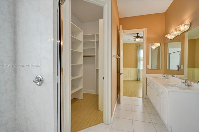 full bathroom featuring a wainscoted wall, a sink, a walk in closet, and tile patterned floors