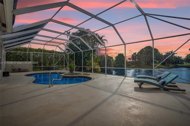 pool at dusk featuring glass enclosure, a patio area, a pool with connected hot tub, and a water view