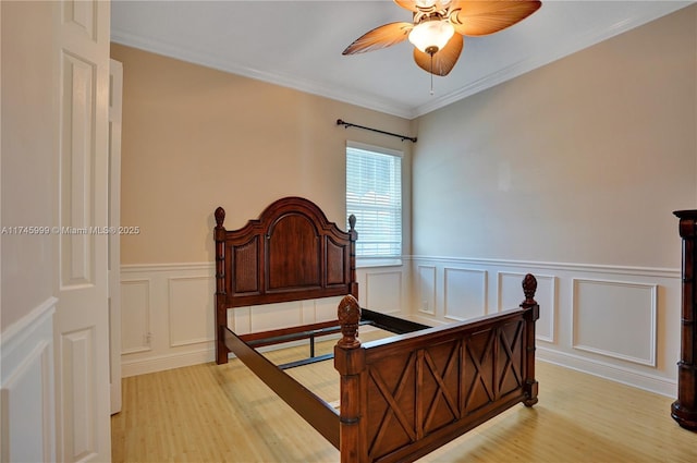 bedroom featuring light wood-style floors, a ceiling fan, crown molding, and a wainscoted wall