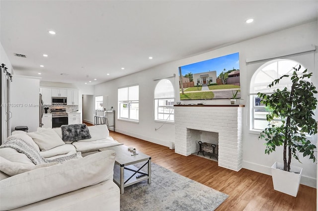 living area with recessed lighting, baseboards, light wood-style floors, visible vents, and a brick fireplace