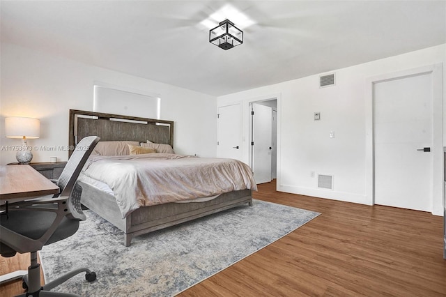 bedroom with baseboards, visible vents, and wood finished floors