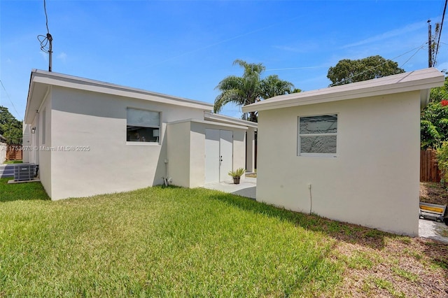 rear view of house with stucco siding, a lawn, and an outdoor structure