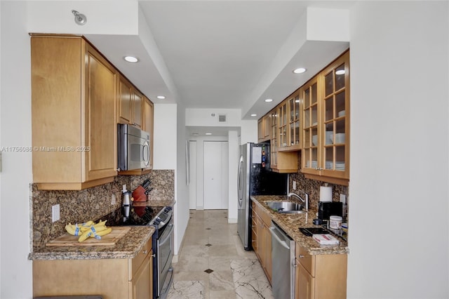 kitchen with light stone counters, stainless steel appliances, a sink, tasteful backsplash, and glass insert cabinets