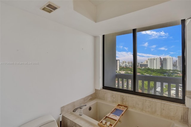 bathroom featuring a jetted tub, a city view, visible vents, and toilet