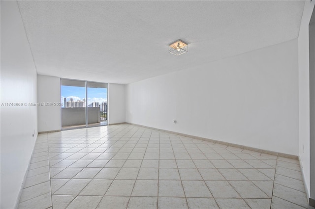 unfurnished room featuring a view of city, expansive windows, light tile patterned flooring, a textured ceiling, and baseboards