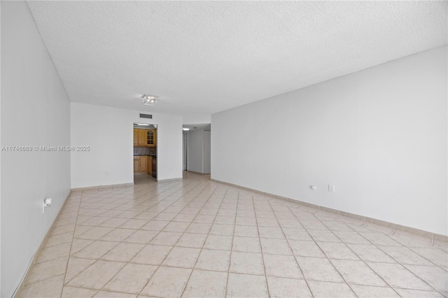 empty room with a textured ceiling, light tile patterned floors, visible vents, and baseboards