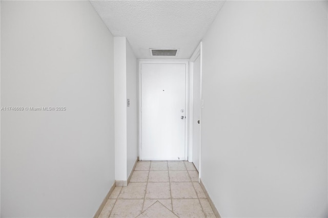 hall with visible vents, a textured ceiling, and baseboards