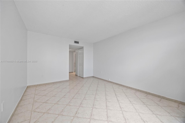 spare room featuring a textured ceiling, visible vents, and baseboards