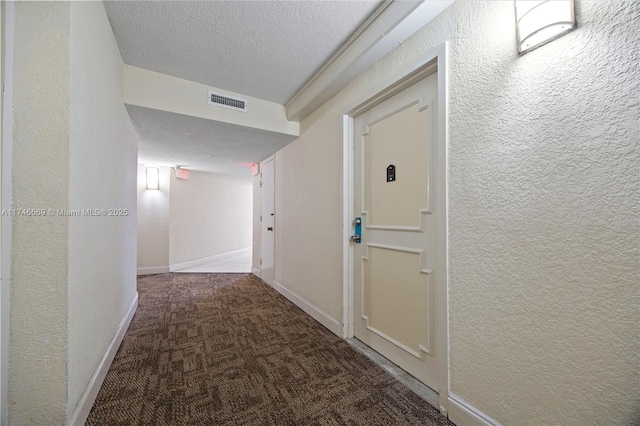 corridor featuring a textured ceiling, a textured wall, visible vents, baseboards, and carpet