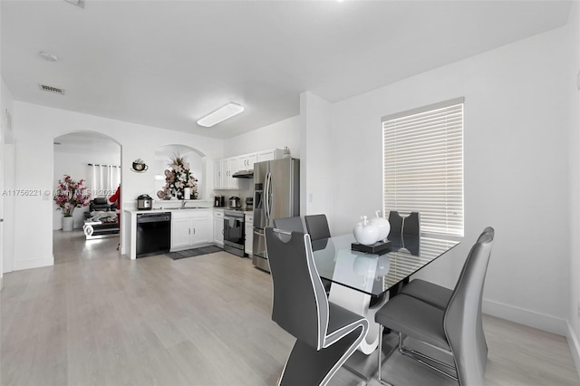 dining area featuring arched walkways, light wood-style flooring, visible vents, and baseboards