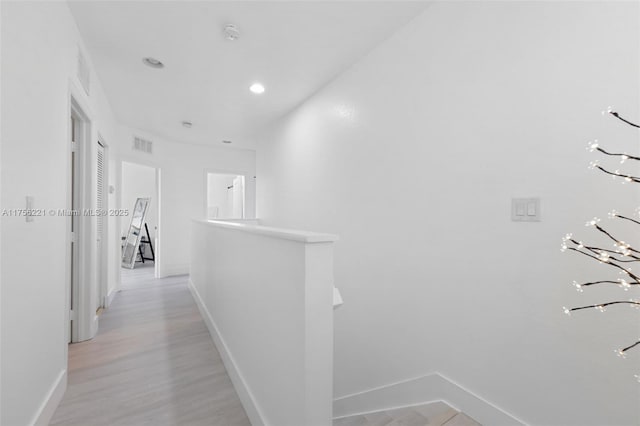 corridor with baseboards, visible vents, light wood finished floors, and an upstairs landing