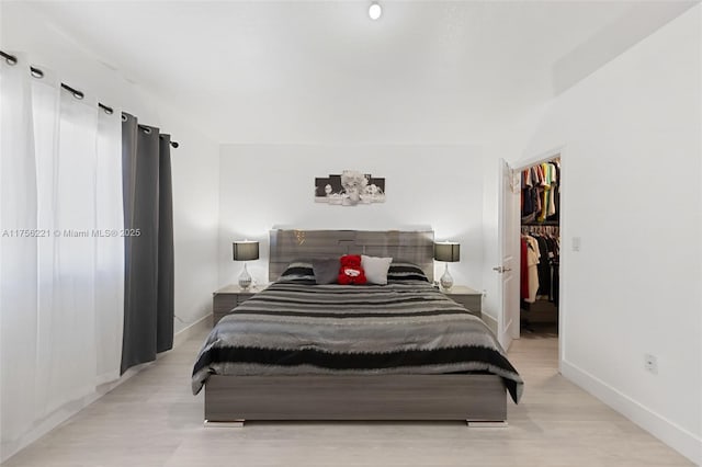 bedroom featuring light wood-style floors, a spacious closet, and baseboards