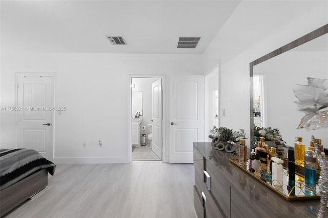 bedroom with light wood-type flooring, baseboards, visible vents, and ensuite bathroom