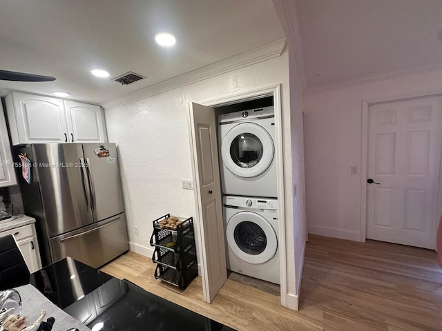 laundry room featuring laundry area, light wood-type flooring, stacked washer and clothes dryer, and ornamental molding