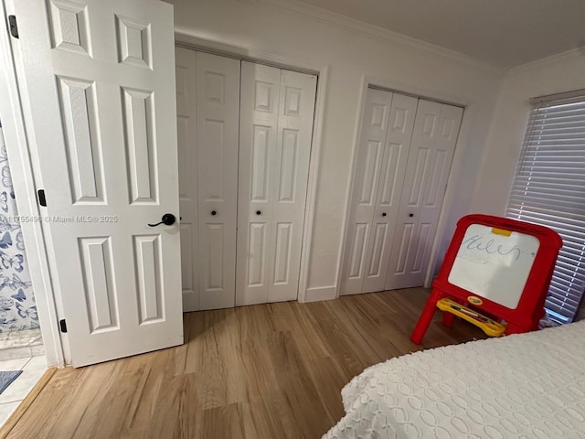 bedroom featuring ornamental molding, baseboards, multiple closets, and wood finished floors