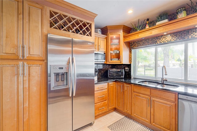 kitchen featuring tasteful backsplash, dark stone countertops, appliances with stainless steel finishes, light tile patterned flooring, and a sink