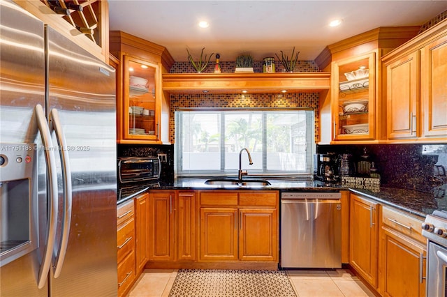 kitchen featuring light tile patterned floors, a sink, stainless steel appliances, glass insert cabinets, and tasteful backsplash