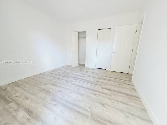 unfurnished bedroom with light wood-style floors, baseboards, and multiple closets