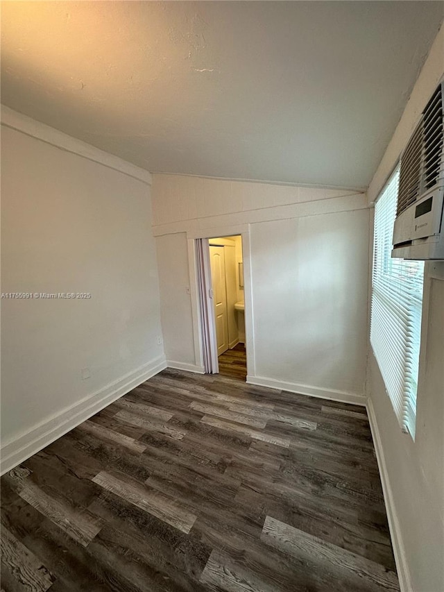 spare room featuring lofted ceiling, baseboards, and dark wood-type flooring